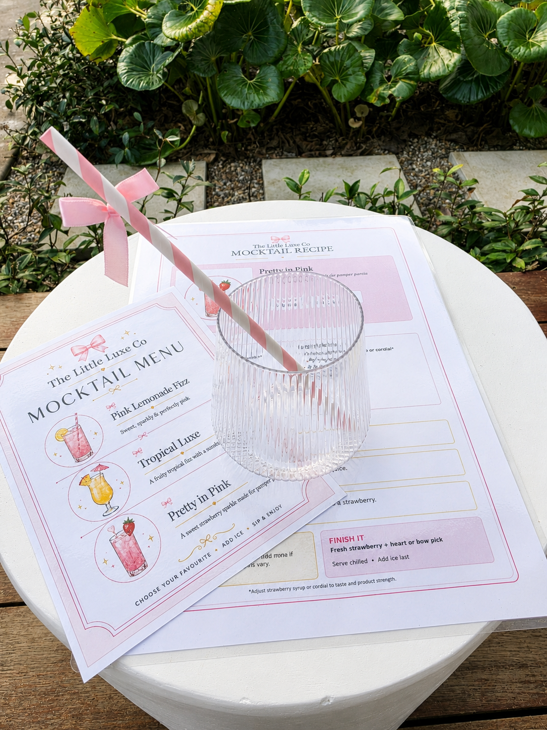 Little Luxe Mocktail Bar Kit with clear glass, pink bow straw, mocktail menu and recipe card styled with greenery.