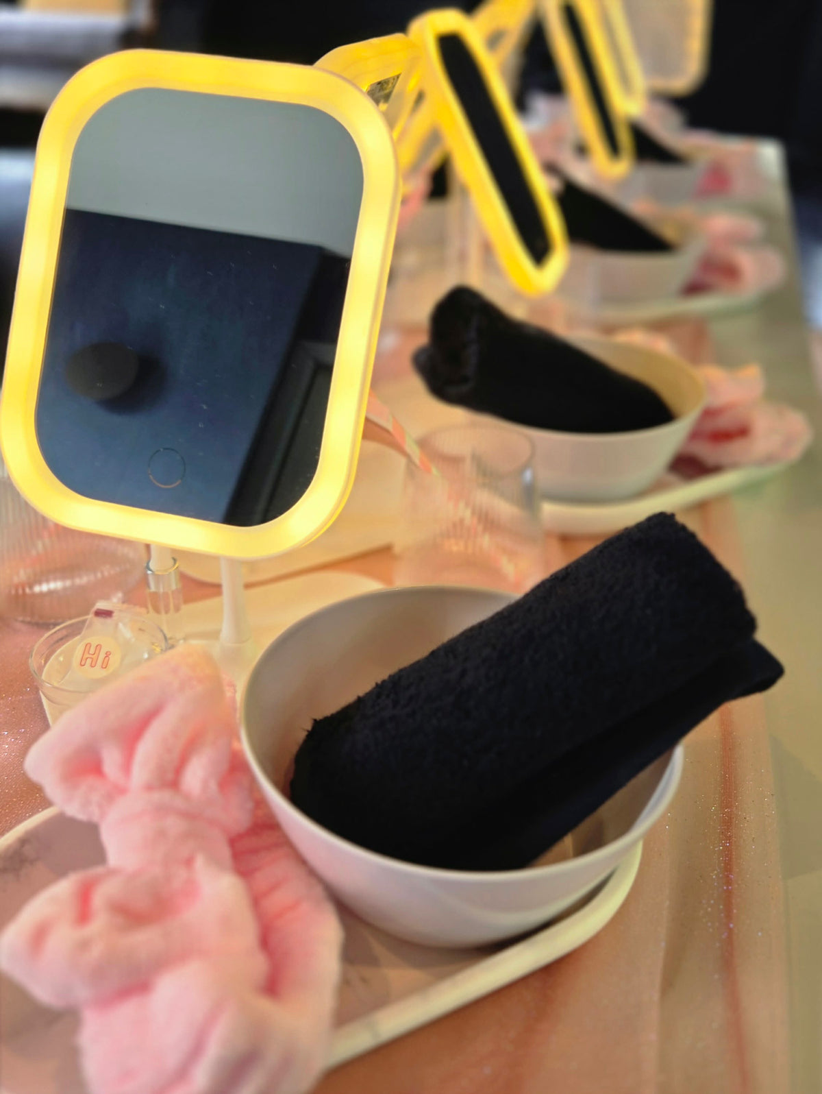Close-up of a Mini Luxe Spa Party place setting with an illuminated mirror, white bowl, navy towel and pink headband.